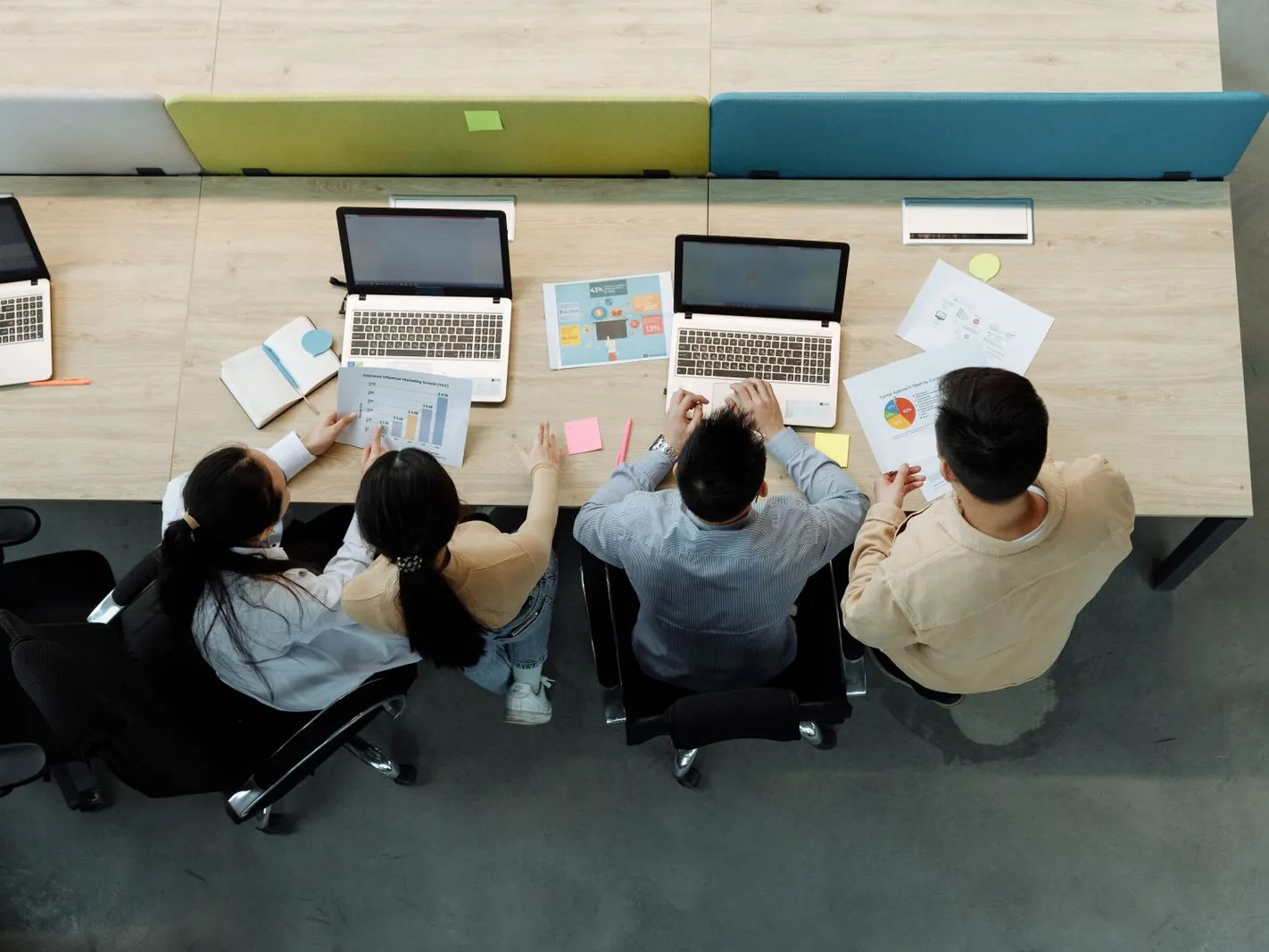 Cuatro compañeros trabajando con laptops en una mesa compartida, vistos desde arriba