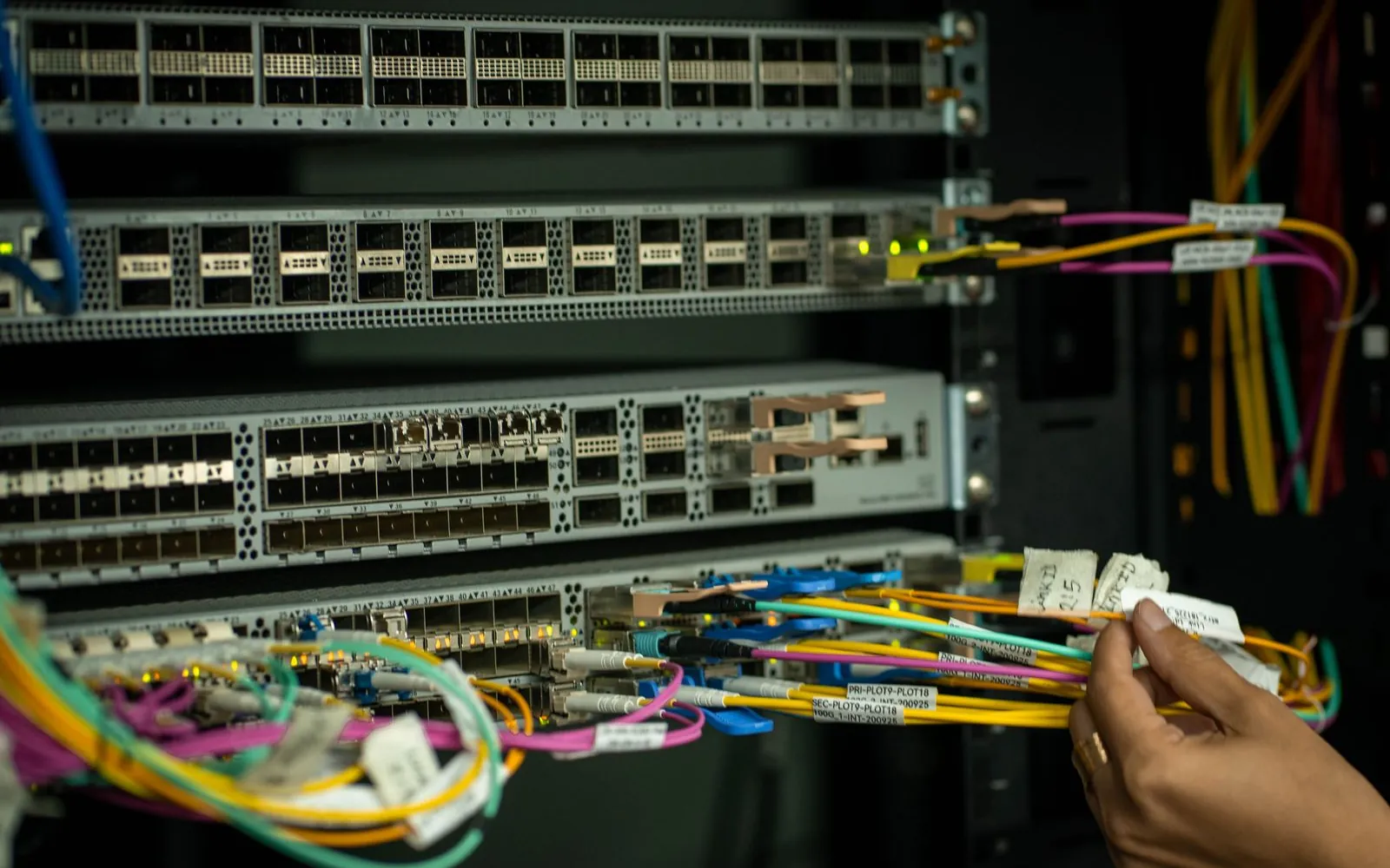Manos conectando cables de fibra en un switch dentro de un rack